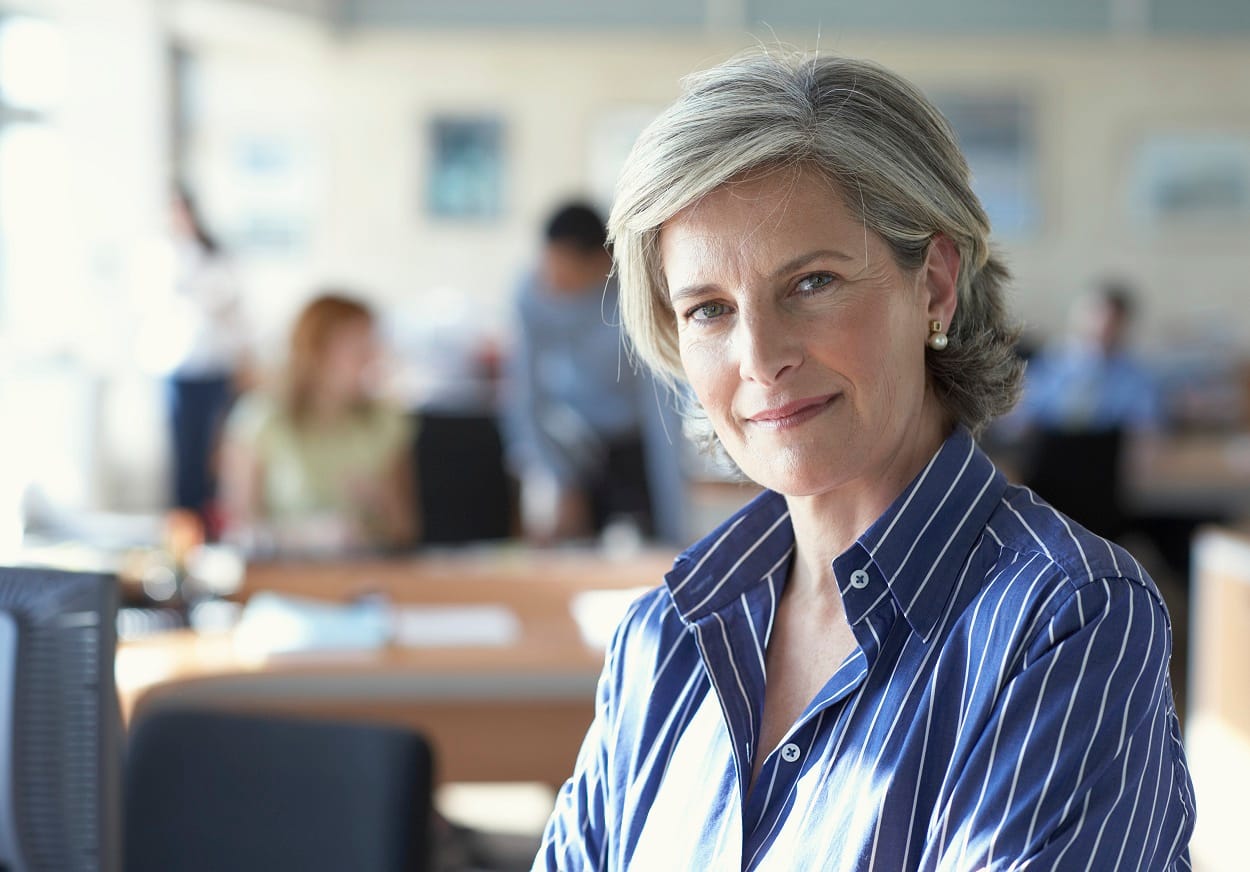 executive woman looking seriously into camera with people in the office behind her