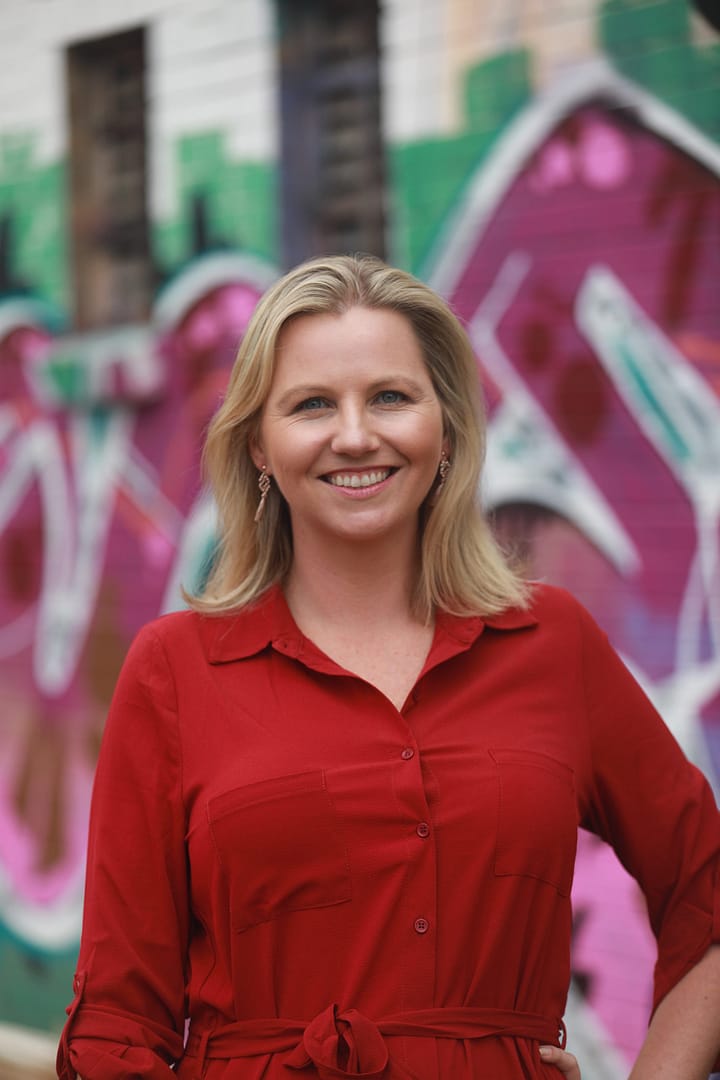 selection criteria writer Nicole wearing a red dress standing against a graffiti wall