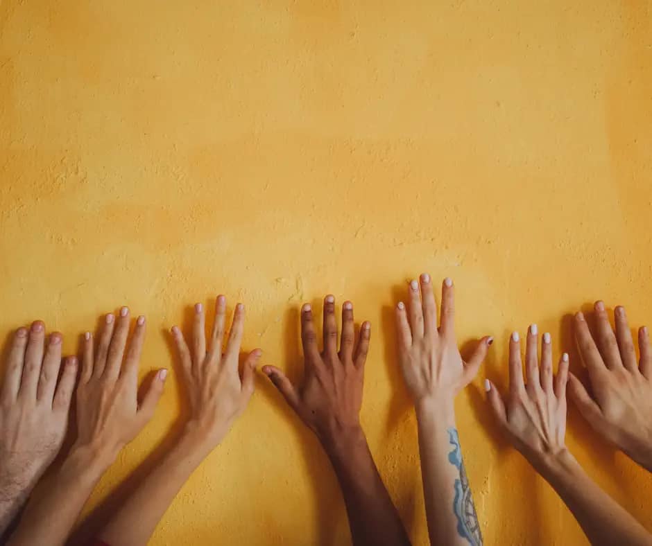 hands with different skin colours lined up on a yellow wall
