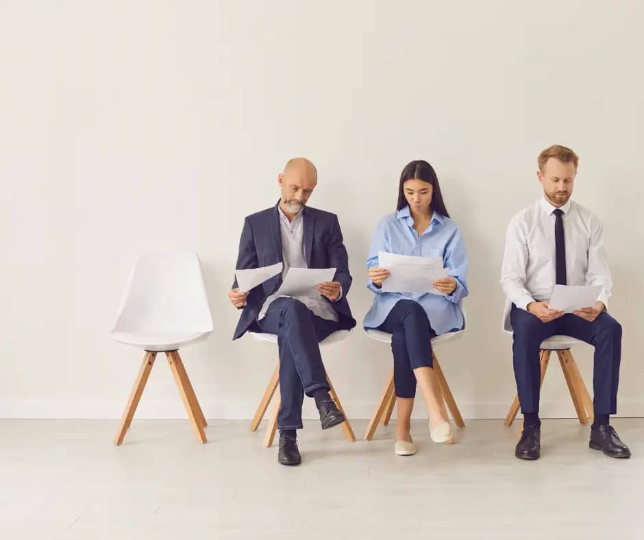 3 professional applicants wait for an interview looking through resume documents