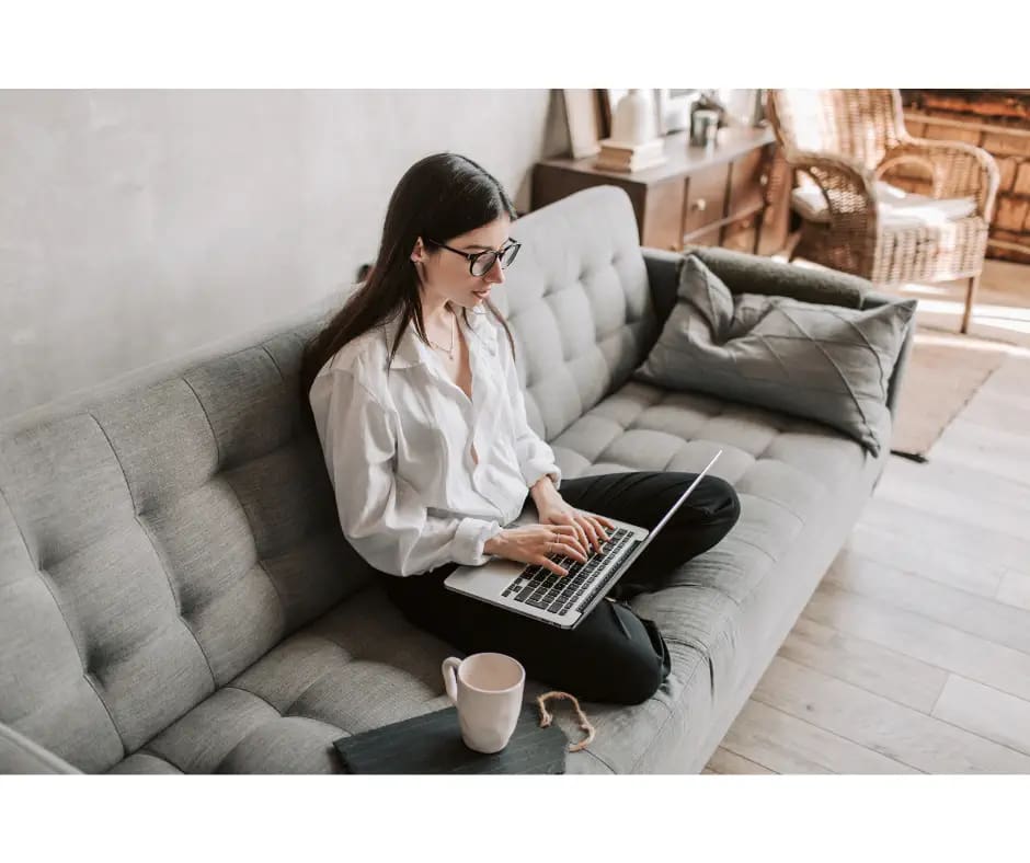 girl sitting on couch typing on a computer with a cup of coffee